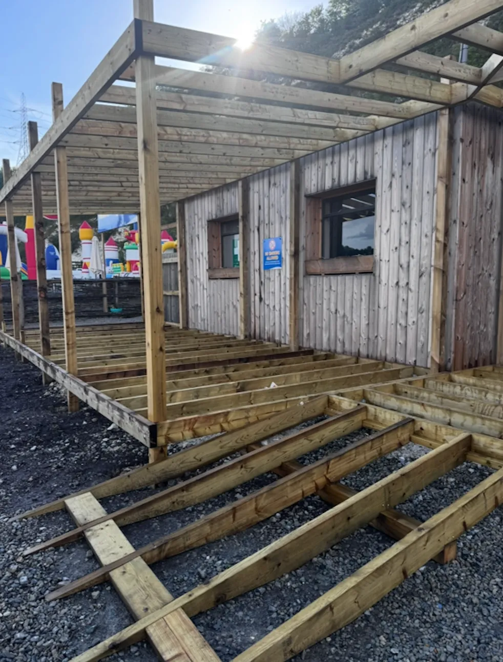 Timber decking joists and framework under construction alongside a clad outbuilding