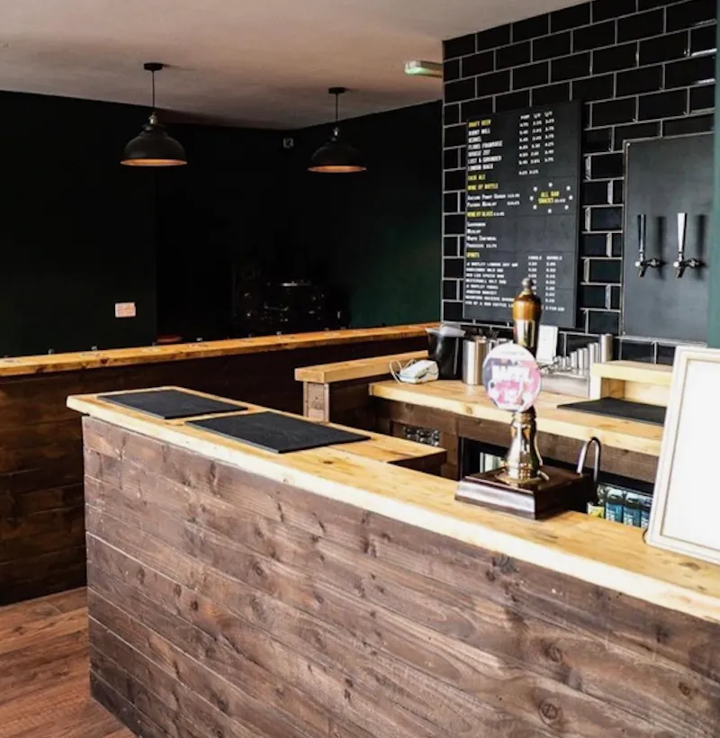 Bespoke timber-clad bar counter with beer pumps, set against a black tiled wall and chalkboard drinks menu