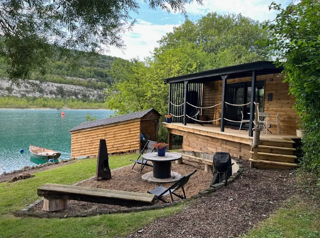 Finished timber-clad container studio with a covered veranda, set on the shore of a lake