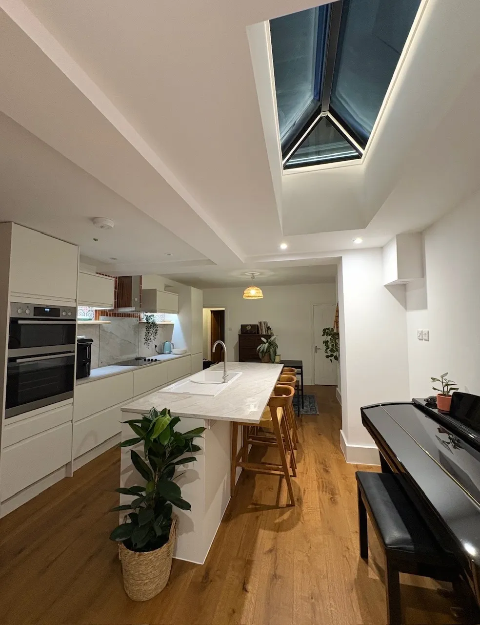 Bright kitchen extension with a triangular roof lantern, exposed timber cladding and an island unit