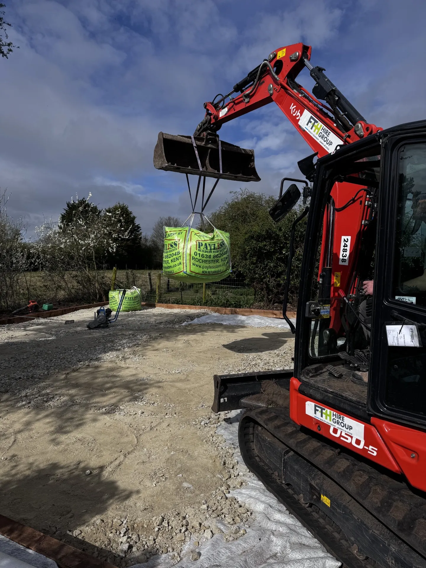 Mini excavator lifting a bulk bag of aggregate onto a prepared hardcore base on a groundworks site in Kent