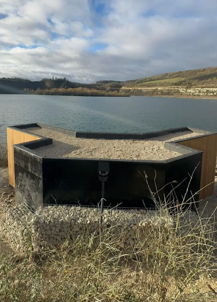 Timber and dark-clad bird hide structure on the shore of a lake, part of a wildlife sanctuary in Rochester